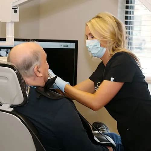 Dental hygienist wearing mask examines male patient's neck in clinical treatment room.