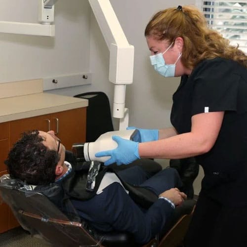 Dental hygienist wearing mask and gloves examining patient's teeth in clinical treatment chair.