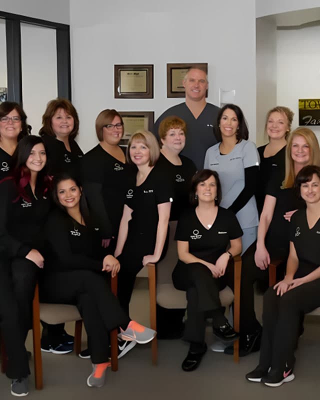 Dental office team in black uniforms posing together in clinical setting.