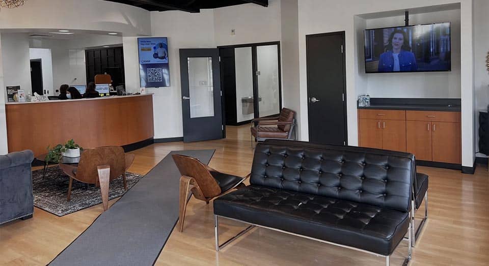 Modern dental office waiting room with black sofa, wooden furniture, and reception desk.