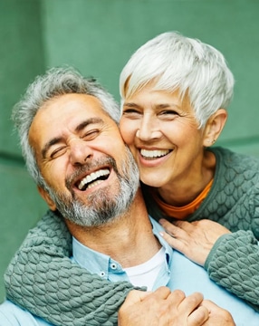 Smiling mature couple embracing outdoors against green background, representing dental care and family wellness.