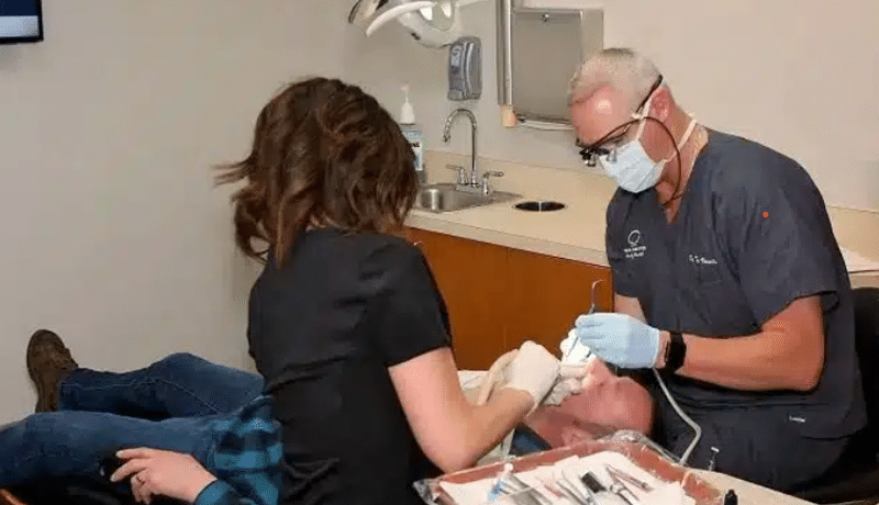 Dentist and assistant examining patient's teeth in modern dental office treatment room.