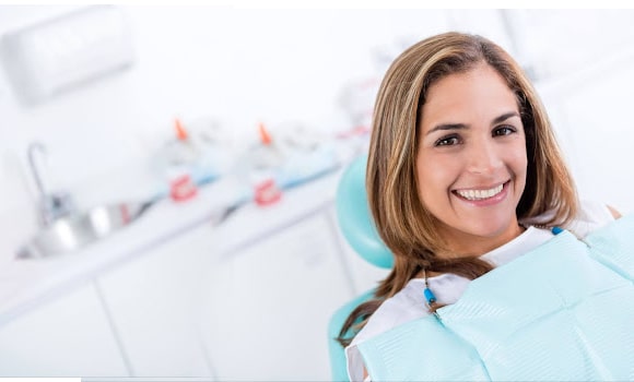 Female dentist in light blue scrubs smiling at camera in modern dental office.
