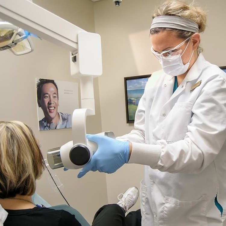 Dentist in white coat and mask holding dental tool during patient examination in dental office.