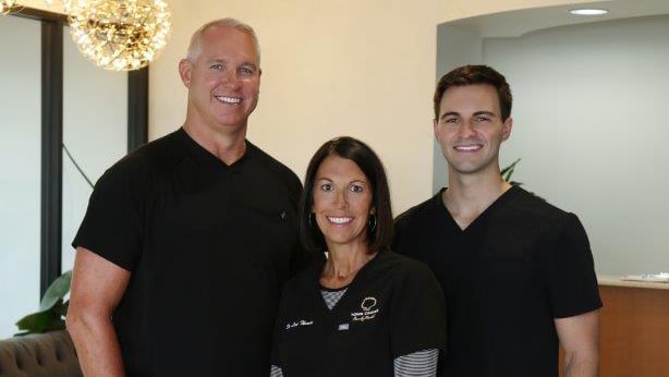 Three dental professionals in black shirts posing together in a modern dental office interior.