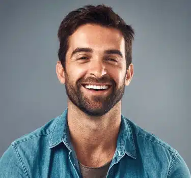 Smiling male dental professional wearing teal shirt against gray background for Town Center Family Dental