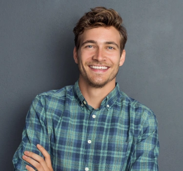 Smiling male dentist wearing blue plaid shirt against gray background for dental practice.