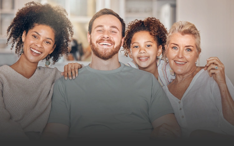 Four diverse adults smiling together in casual clothing against a neutral indoor background.