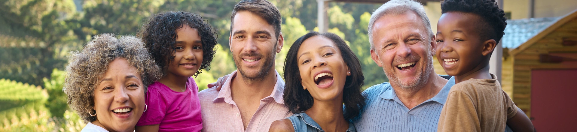 Diverse group of smiling people standing together outdoors in a sunny garden setting.