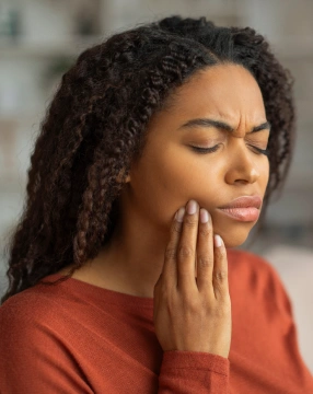 Woman in red shirt holding cheek, appearing to experience tooth pain or discomfort.