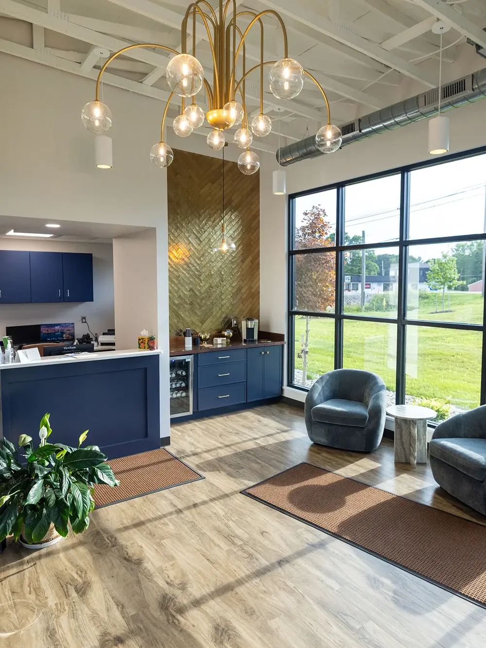 Modern dental reception area with navy cabinetry, gold pendant lighting, and comfortable seating near large windows.