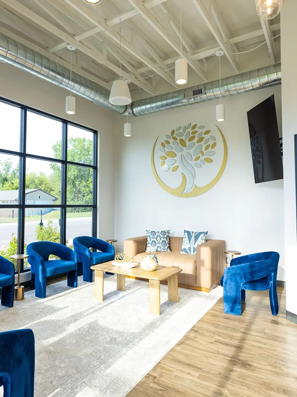 Modern dental waiting room with blue velvet chairs, beige sofa, and natural light in Flint, MI.