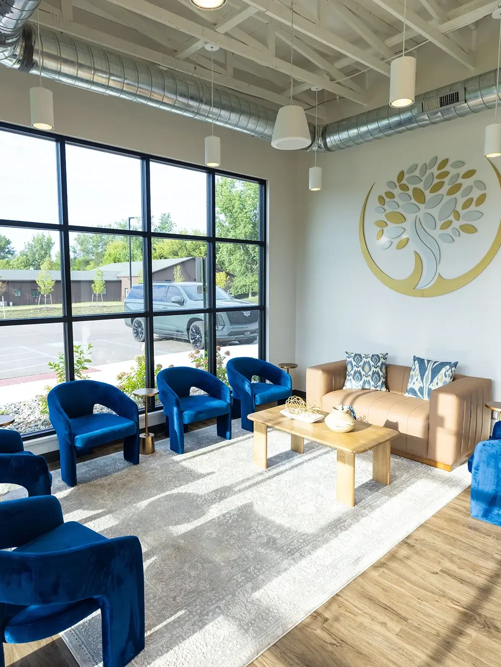 Modern dental waiting room with blue velvet chairs, beige sofa, and natural light in Flint, Michigan.