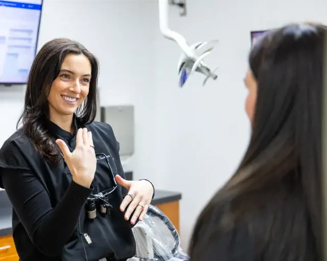 Female dentist smiling while conversing with patient in modern dental office treatment room.