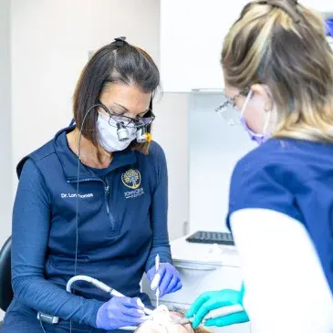 Dental professional in blue scrubs and mask preparing emergency treatment supplies for patient care.