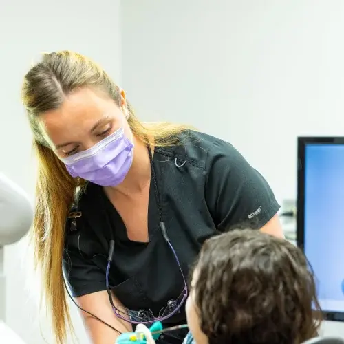 Female dental professional wearing purple mask examining young patient during cosmetic dentistry consultation.