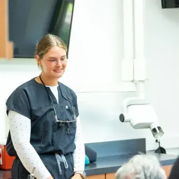 Female dental professional smiling in treatment room with dental microscope at Flint, MI practice.
