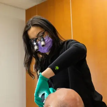 Dentist in protective gear performing emergency dental treatment on patient.
