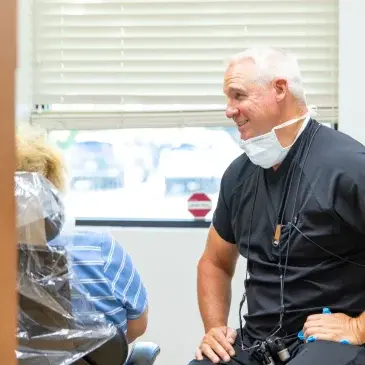 Dentist in black scrubs and mask consulting with patient during preventative dental exam.